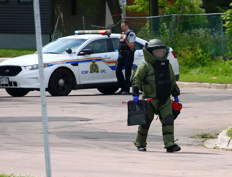 An EDU Member wearing a bomb suit carries equipment away from a scene in Moncton, NB.